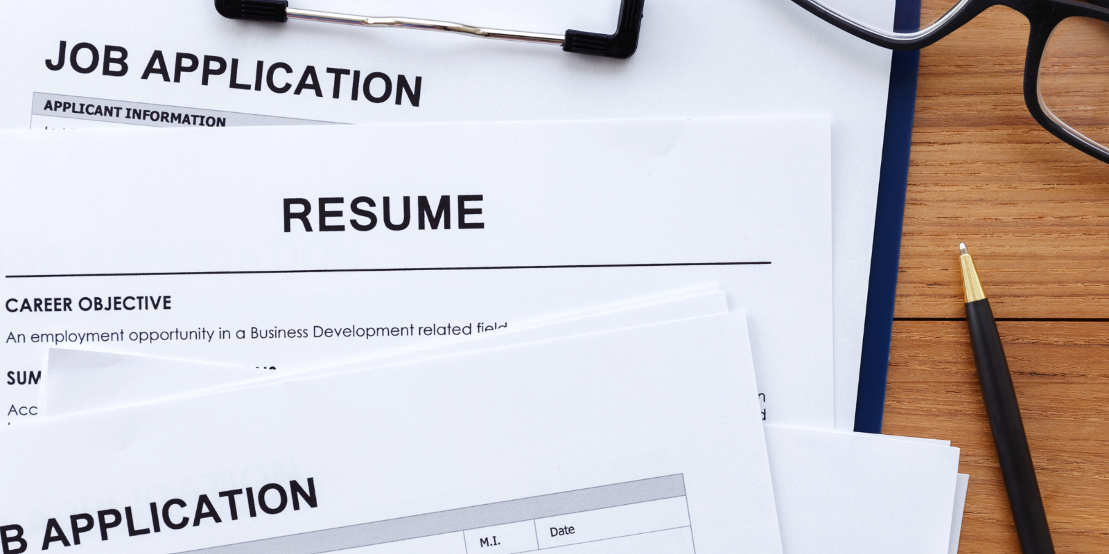 Job application and resume documents with a pen and glasses on a wooden table.