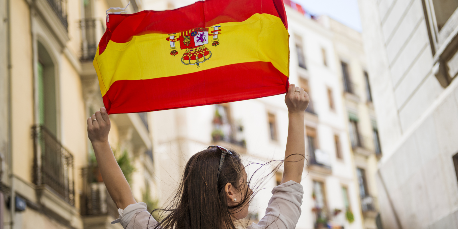 A person holding up the Spanish flag high on a city street.