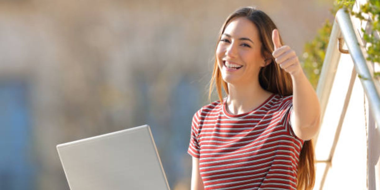 Happy woman with a laptop gesturing thumbs up sitting outdoors