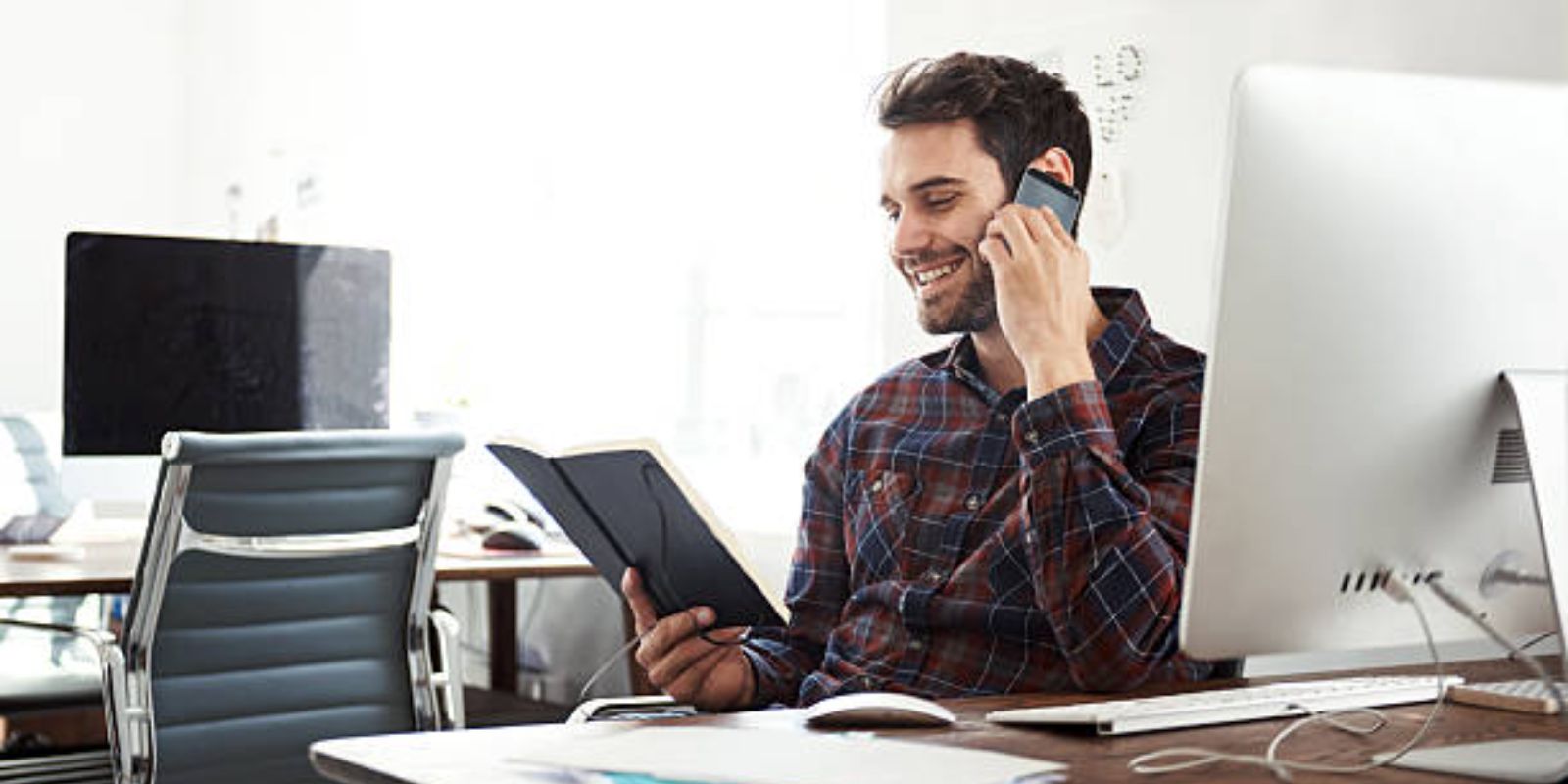 A man talking on his phone while looking at his notebook.