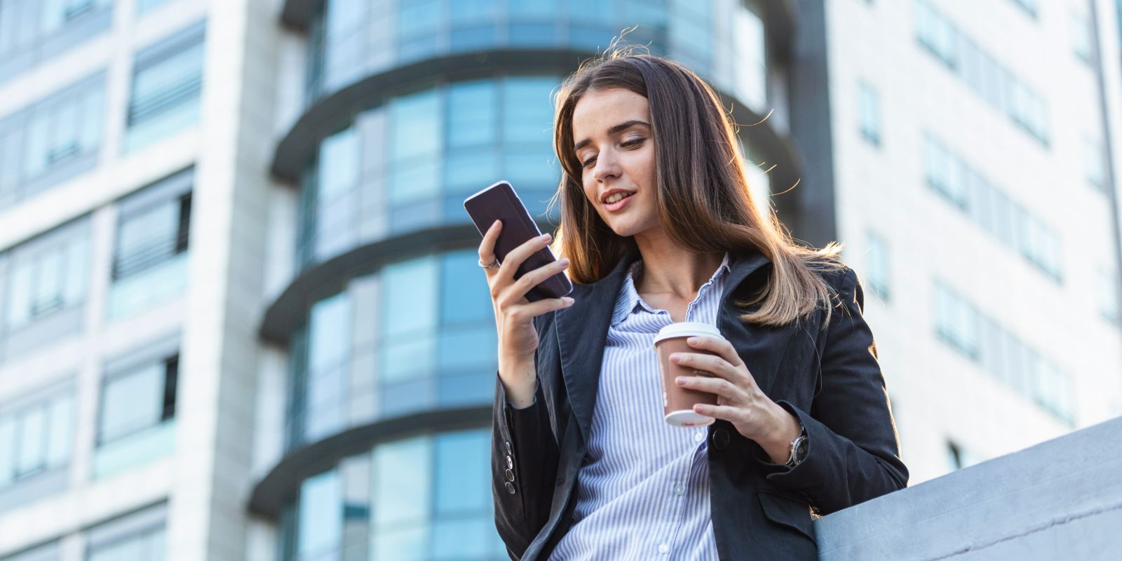 A woman texting on her mobile phone while drinking coffee.